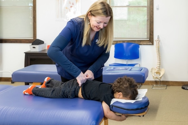 Boy toddler lying facedown on the table being adjusted by Dr. Annie Jackman